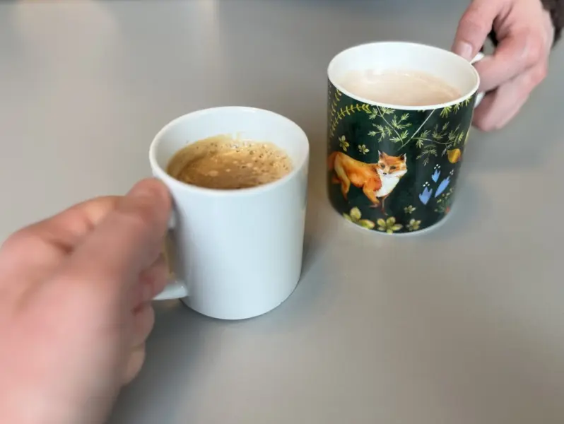 Two hands, each holding mugs, one white and the other bearing the image of a fox