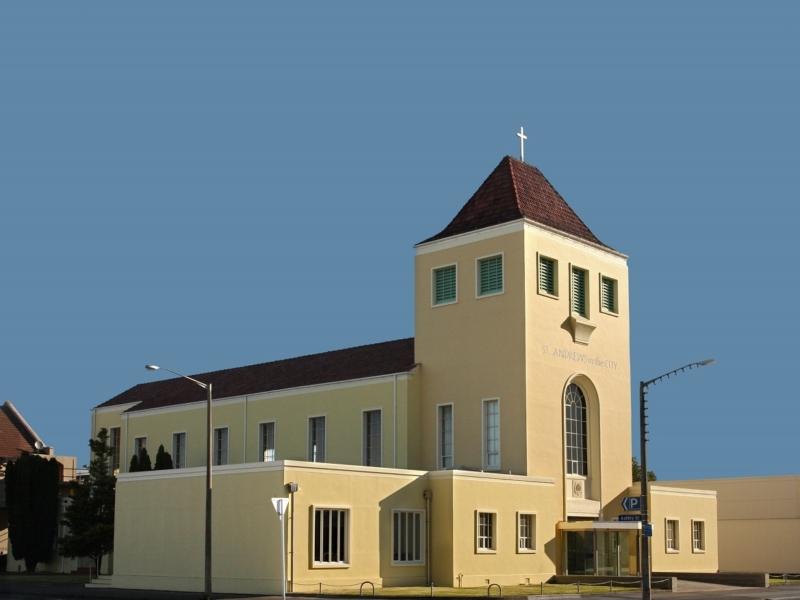 Yellow church building with terracotta tile roof, blue sky background.