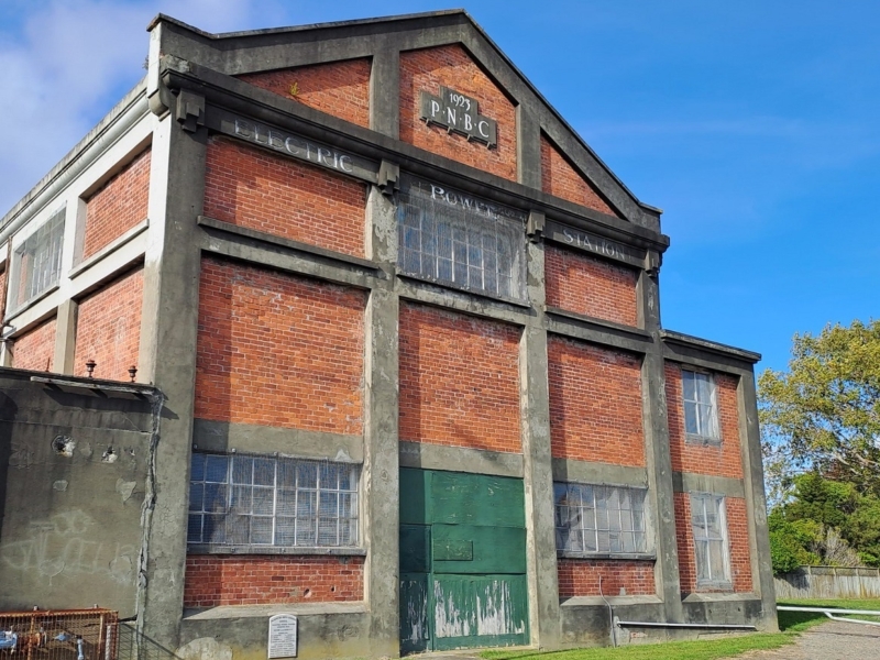 Tall brick building with concrete pillars. Green barn door at bottom.