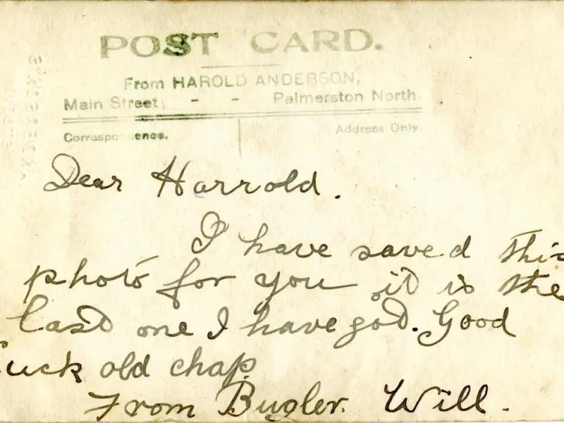 A faded postcard with a message that reads "Dea Harold, I have saved this postcard for you - it is the last one I have got. Good luck old chap. From Bugler Will".