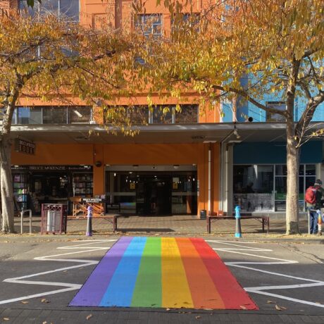 Rainbow crossing with yellow and orange autumn leaves in front of orange and blue facade of the library.