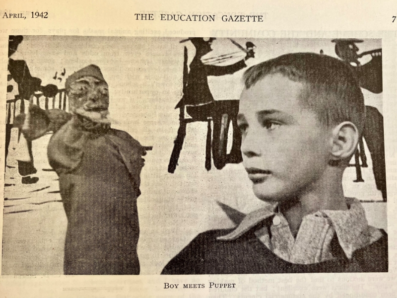 Newspaper clipping of boy in jumper with collared shirt underneath and short cropped hair holding a hand-made puppet.