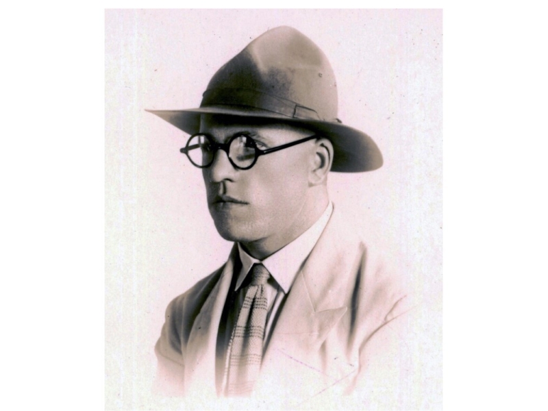An old photographic portrait of an unsmiling man wearing round, black-rimmed spectacles, a campaign hat, and a suit and tie. He is posed at a 3 quarter angle.