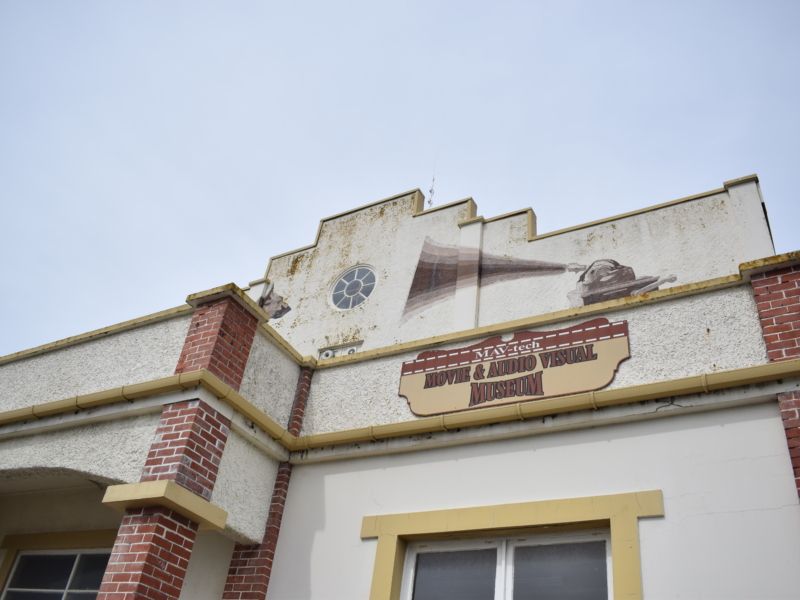 Image of a white building with red brick quoin work and yellow trim.