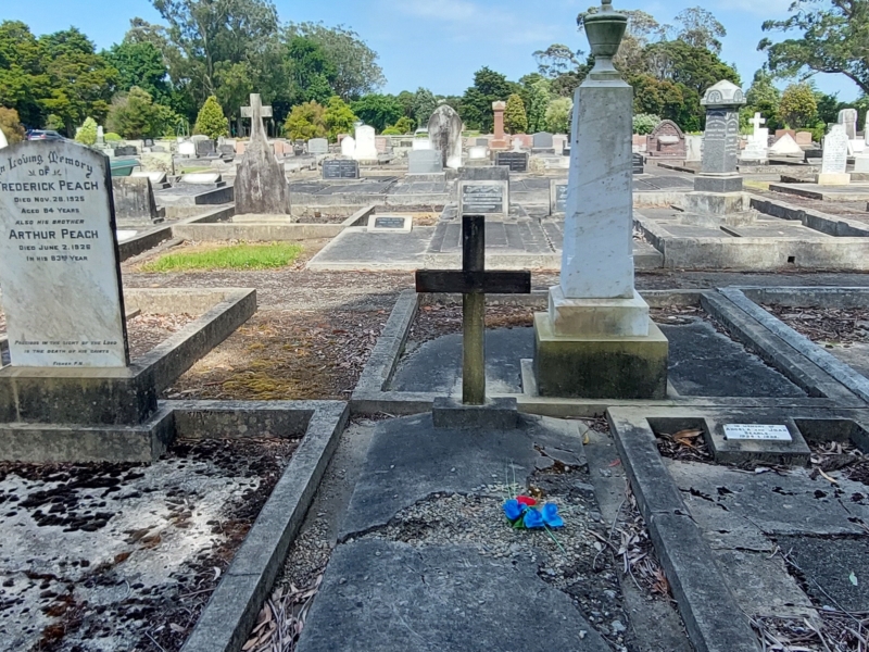 Photo of a graveyard with white and red stone headstones of various sizes and ages and most graves encased in concrete.