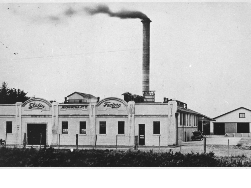 Black and white photo of a white Glaxo factory building and large smokestack with black smoke.