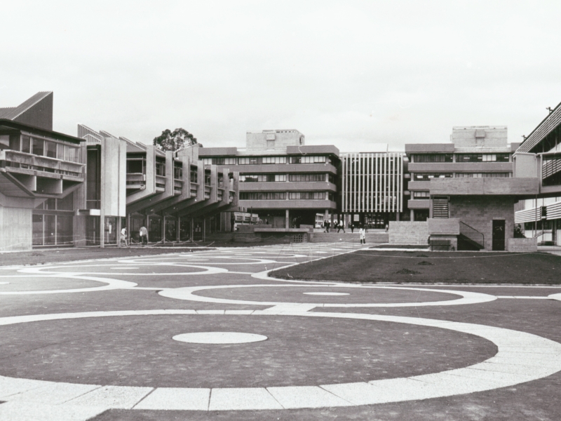 Black and white photograph of a concrete courtyard with brutalist buildings in the background.