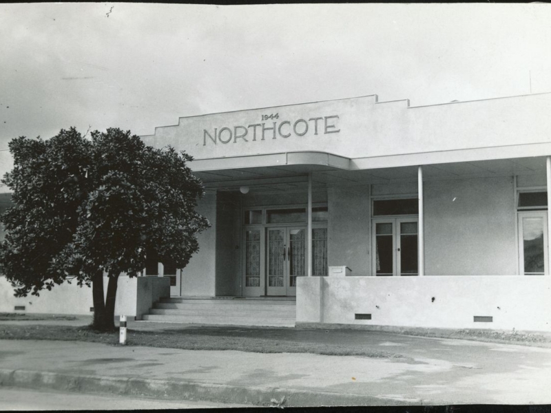 Black and white image of a white art deco building with Northcote at the top. A Pohutukawa tree on the left hand side.