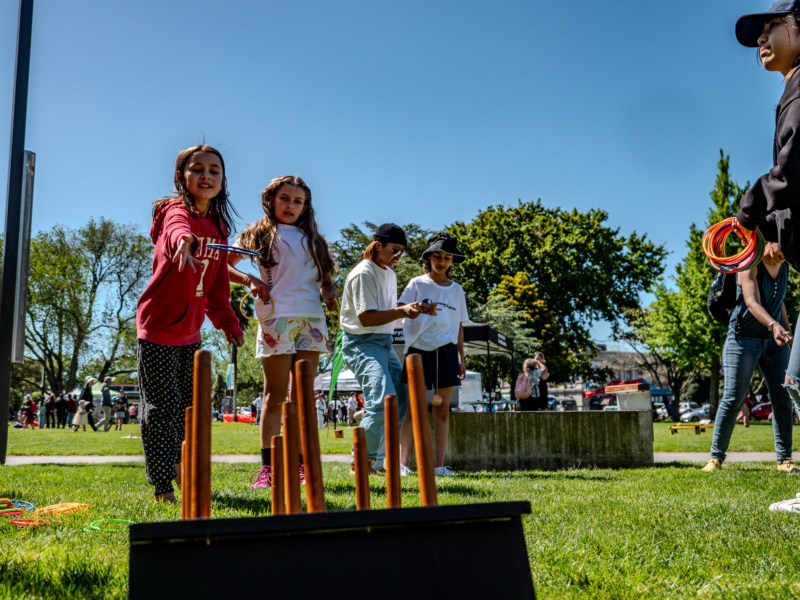 Two young girls one in red one in white toss rings to try to get them on a pegged board on the grass with trees in the background.