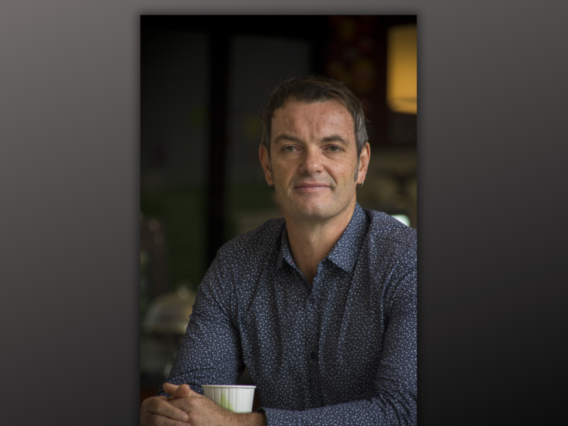 Photo of Richard Shaw sitting, wearing a dark blue shirt holding a cup.